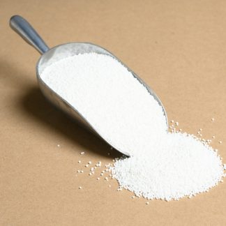 A spoon full of white sugar on a beige background.