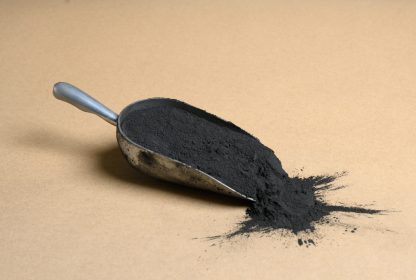 A scoop of black powder on a beige background.