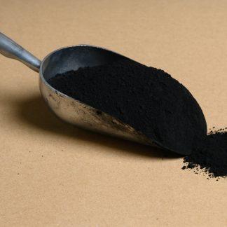Black powder in a metal scoop on a beige background.