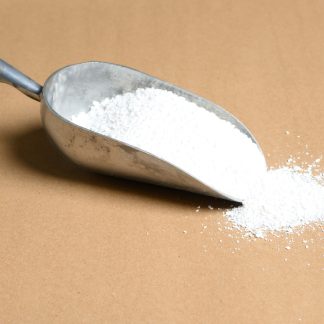 A scoop of Potassium-Benzoate white powder on a brown surface.