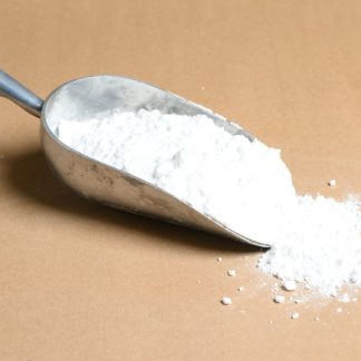 A scoop of ptasium nitrate white powder on a brown surface.