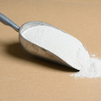 A scoop of Sodium-Oxalate white powder on a brown surface.